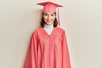 Young caucasian woman wearing graduation cap and ceremony robe with a happy and cool smile on face. lucky person.