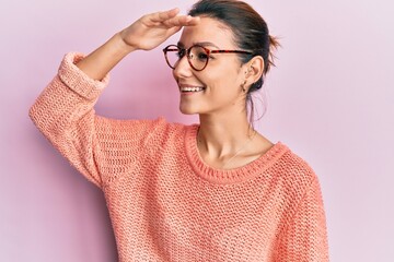 Young caucasian woman wearing casual clothes and glasses very happy and smiling looking far away with hand over head. searching concept.