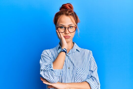 Young beautiful redhead woman wearing casual clothes and glasses over blue background thinking looking tired and bored with depression problems with crossed arms.