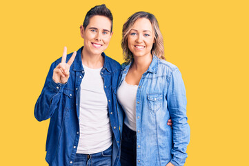 Couple of women wearing casual clothes showing and pointing up with fingers number two while smiling confident and happy.