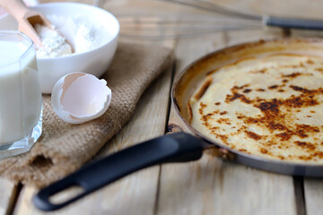 Frying pan with pancake, flour, milk, eggs. Pancake making concept. Maslenitsa celebration.