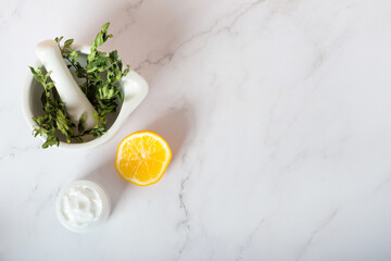 herbs in a mortar, soap and cream with lemon on a white background