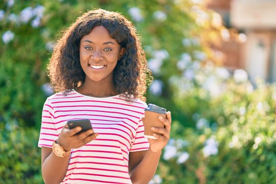 Young african american girl using smartphone drinking coffee at the park.