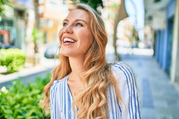 Young beautiful caucasian woman with blond hair smiling happy and cheerful walking on sunny day