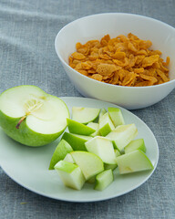 Bowl of cornflake in white container and chopped green apple ,Signifying healthy breakfast