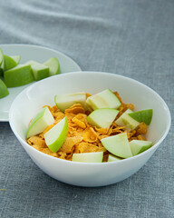 Bowl of cornflake in white container and chopped green apple ,Signifying healthy breakfast