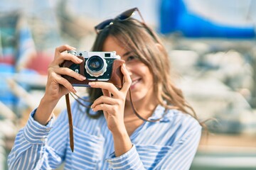 Young hispanic tourist woman smiling happy using vintage camera at the port.