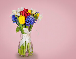 glass vase with spring flowers on pink background. copy space