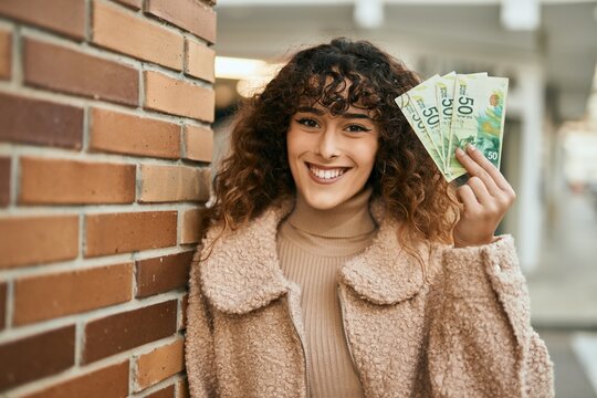 Young hispanic woman smiling happy holding israel shekels banknotes at the city