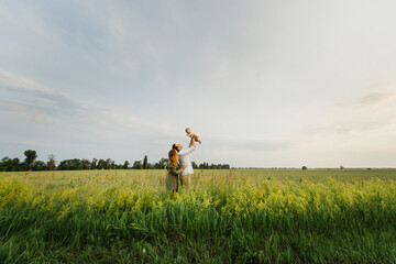 Young parents hug and kiss their newborn daughter in nature.
