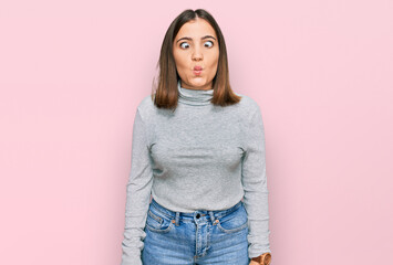 Young beautiful woman wearing casual turtleneck sweater making fish face with lips, crazy and comical gesture. funny expression.