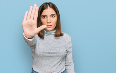 Fototapeta premium Young beautiful woman wearing casual turtleneck sweater doing stop sing with palm of the hand. warning expression with negative and serious gesture on the face.