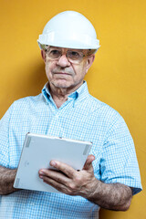 Man in a white shirt and engineer helmet holding a tablet with a yellow background.
