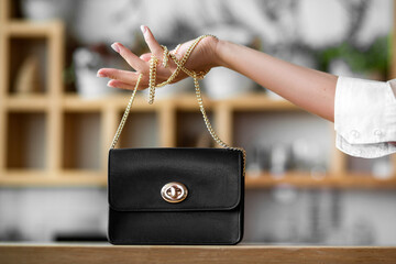 a woman's hand holds a small black bag on a chain in the office
