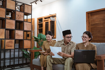 two female civil servants and a male civil servant sit using laptop computers and worksheets while...
