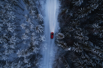 Red car driving on winter mountain road at night time. Beautiful aerial view with the trees covered in snow. Light in the dark. 
 - Powered by Adobe