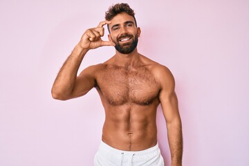 Fototapeta premium Young hispanic man standing shirtless smiling and confident gesturing with hand doing small size sign with fingers looking and the camera. measure concept.