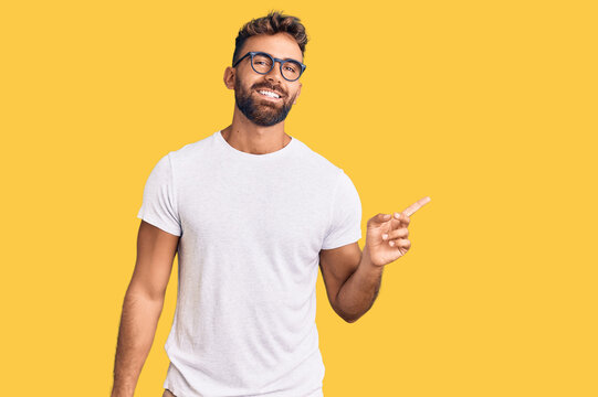 Young hispanic man wearing casual clothes and glasses with a big smile on face, pointing with hand finger to the side looking at the camera.