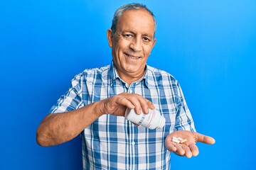 Senior hispanic man holding pills smiling with a happy and cool smile on face. showing teeth.