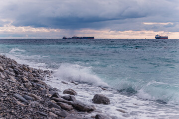 The tanker ship sails on the sea horizon. Stone coast and sea waves in the foreground