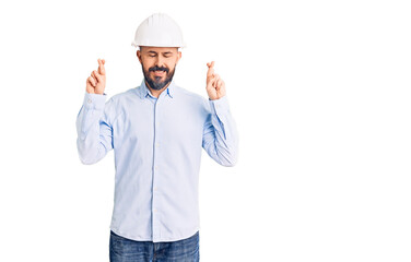 Young handsome man wearing architect hardhat gesturing finger crossed smiling with hope and eyes closed. luck and superstitious concept.