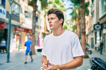 Young caucasian man with serious expression smoking cigarette at the city.