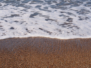 Blue sea, white wave and brown sand on the beach with shells and stones, Alanya, Turkey. Copy space for text.