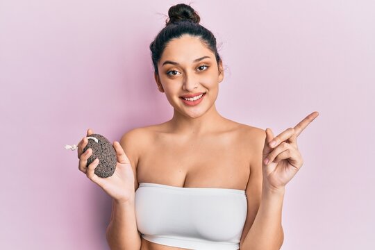 Beautiful middle eastern woman holding pumice stone smiling happy pointing with hand and finger to the side