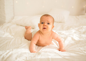 upset little baby girl in a diaper lying on her stomach on the bed