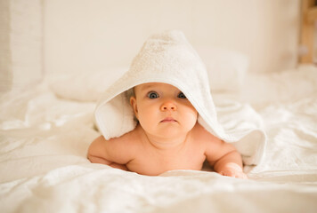 a little baby girl in a white bath towel lies on the bed and looks at the camera