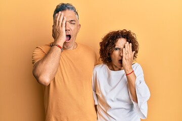 Beautiful middle age couple together wearing casual clothes yawning tired covering half face, eye...