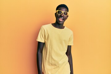 Young african american man wearing casual clothes and glasses winking looking at the camera with sexy expression, cheerful and happy face.