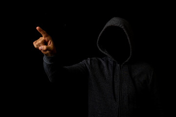 Man without a face in a hood touches his finger on a dark background