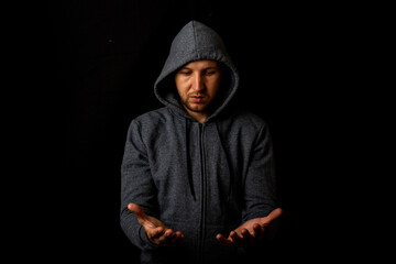 Man in a hood holds something in his hands on a dark background