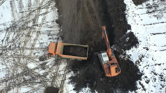 The excavator digs a pit and loads the soil into a dump truck. Drone video.