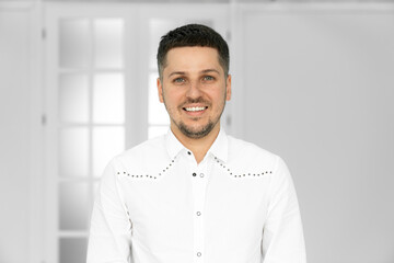 Happy smiling young Hispanic businessman standing in office looking at camera