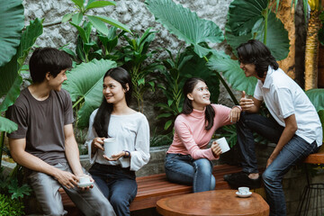 two couples chatting in the garden holding cups sitting on wooden chairs