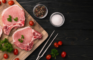 Meat steaks. Raw pork or beef ribeye meat with bone. Ingredients for barbecue. Cherry tomatoes, colored pepper, sea salt and parsley on black wooden background. Veal chunk. Food photography.