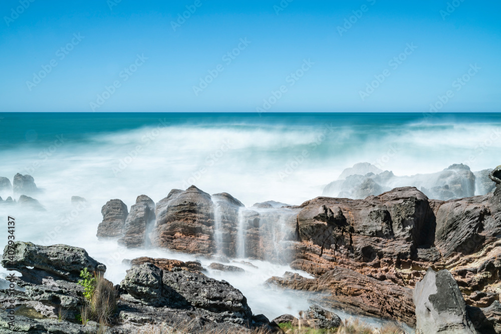 Poster whitewater from surf smoothed as it breaks around rugged coast at base of mount maunganui, new zeala