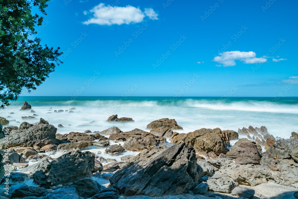 Poster whitewater from surf smoothed as it breaks around rugged coast at base of mount maunganui, new zeala