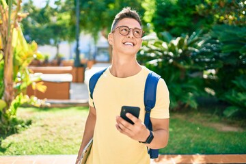 Young hispanic student smiling happy using smartphone walking the university campus