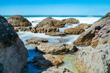 Whitewater from surf smoothed as it breaks around rugged coast at base of Mount Maunganui, New zealand