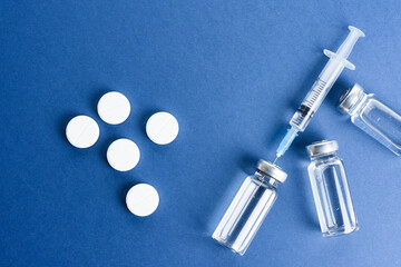 Medical ampoules with vaccine and pills on a blue background.
