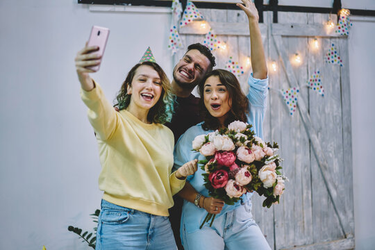 Carefree young hipsters having fun on anniversary celebration shooting video on cellular for share in blog, emotional male and female best friends posing for selfie on smartphone camera enjoy party