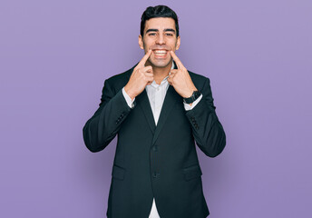 Handsome hispanic man wearing business clothes smiling with open mouth, fingers pointing and forcing cheerful smile