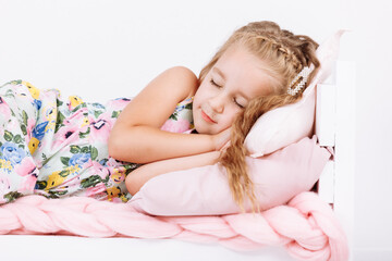 Naklejka premium Bedtime. Little girl is sleeping in the bed. Soft bed with pink linen in white bedroom. Child sleep regime hours, daily routine. Sweet dreams concept.