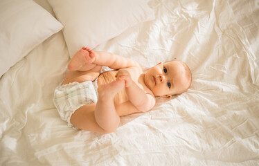 a little baby girl in a diaper lies on the bed and looks at the camera