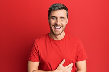 Handsome caucasian man wearing casual red tshirt smiling and laughing hard out loud because funny crazy joke with hands on body.