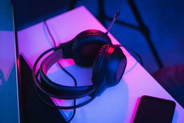 High angle shot of gaming headphones and a phone on a desk under colorful led lights in a dark room © Eduardo Sandoval/Wirestock