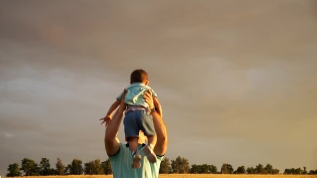 Happy father is throwing his son in the air and catches him at the field. The man is playing with his kid at the outdoors in summer. The conception of family leisure at the open air.